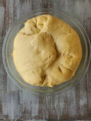 Dough in a clear bowl that has fully risen and is ready to be rolled out