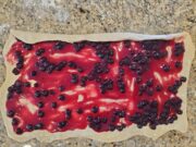 Rectangular dough spread with Blueberry sauce being rolled up.