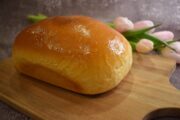 Loaf of Amish White Bread resting on a wooden cutting board with some pink tulips in the background