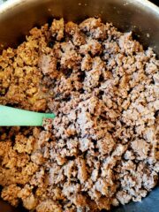 Pan of ground beef fried in a pan with a blue spatula.