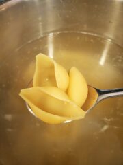 Spoon with 3 jumbo shells over a pot of water.