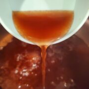A cup of pickling liquid being poured into a boiling pot.