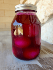A jar of red beet eggs on a wood surface.